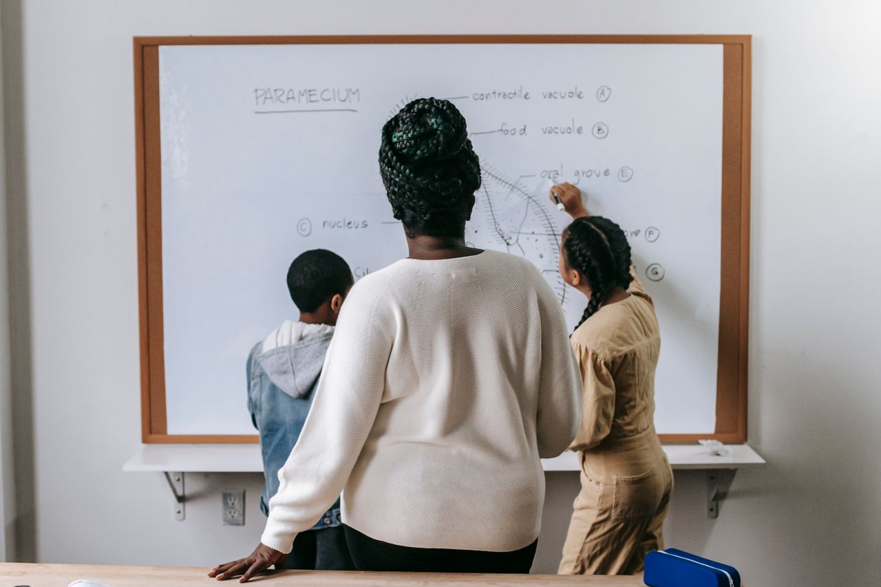 Teacher watching attentively as students write on the whiteboard in class